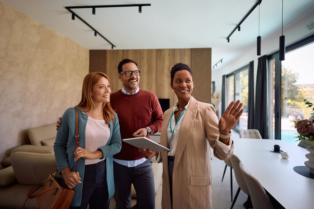 Happy African American real estate agent using digital tablet while showing new house to a couple.