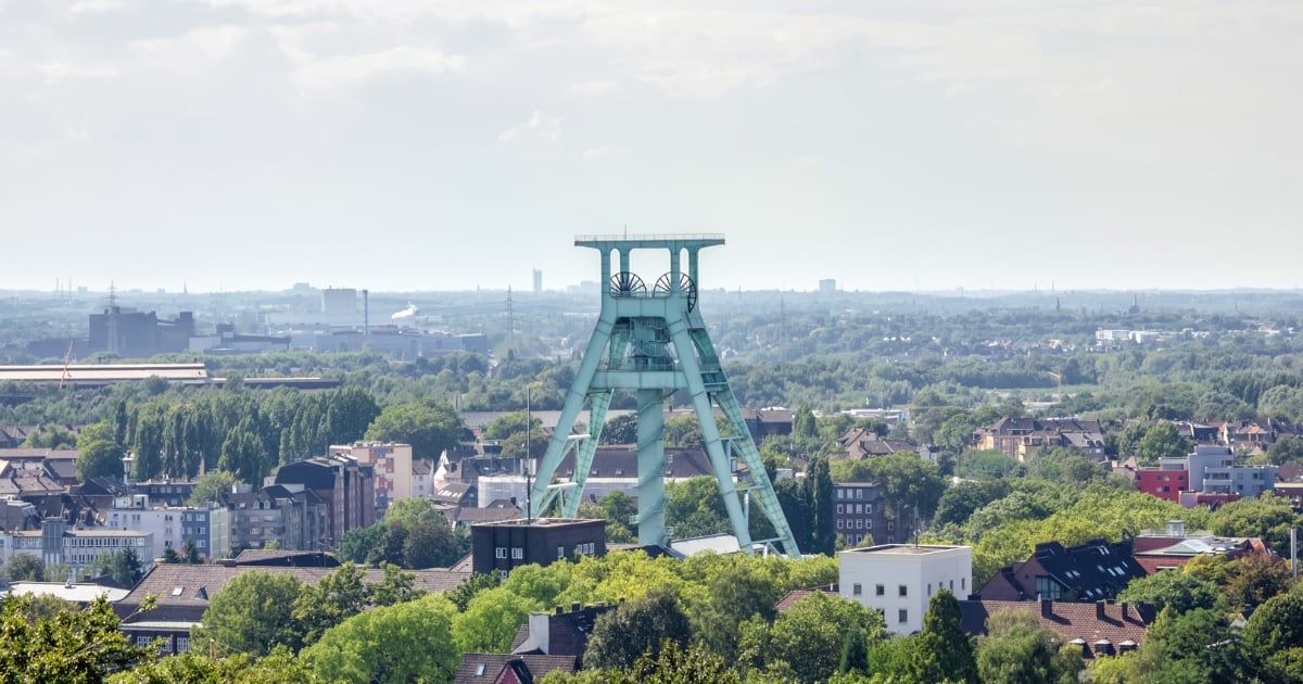 Historic mining headframe overlooking an urban landscape with buildings, trees, and expansive cityscape in background