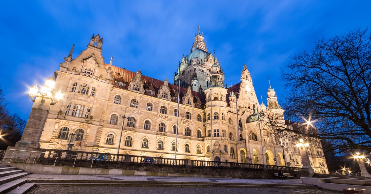 Illuminated Gothic Revival castle at dusk with ornate architecture and multiple spires against a blue twilight sky